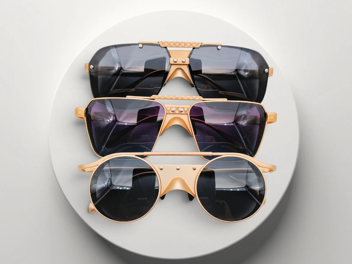 Three custom metal sunglasses with gold-tone frame details and varied lens shapes displayed on a round white platform