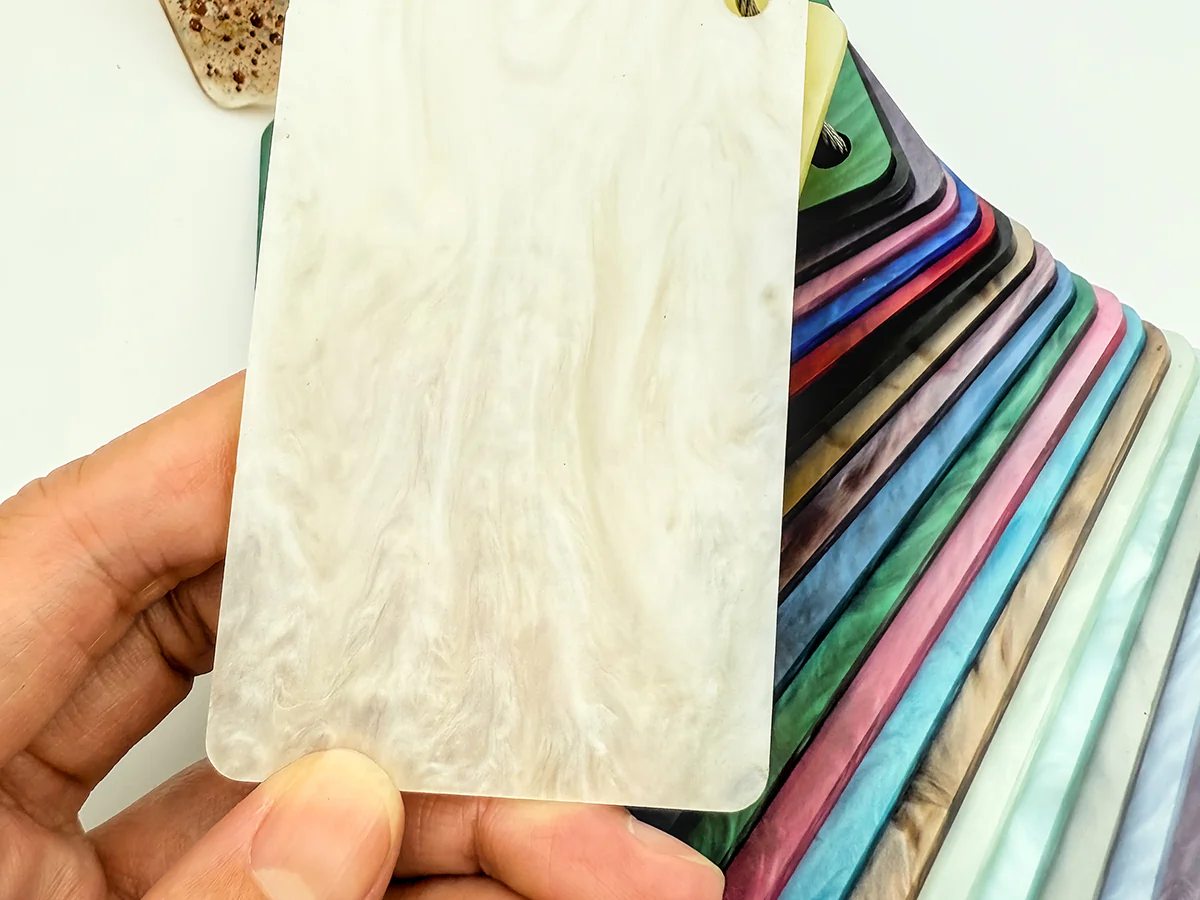 Hand holding an ivory marbled acetate sample in front of a range of colorful eyewear material swatches