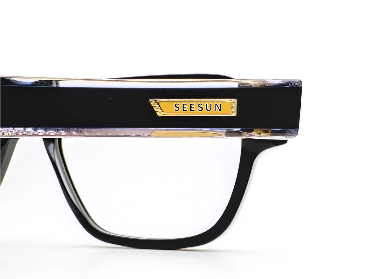 Close-up of a metal logo plaque set into a black acetate eyeglass frame.