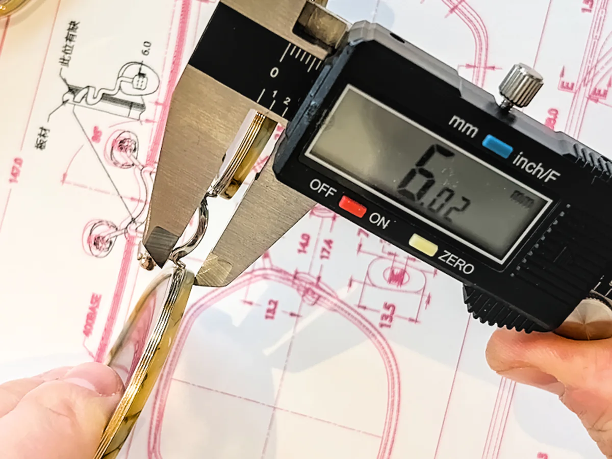 Digital caliper measuring a gold-tone metal eyewear component over a technical frame drawing