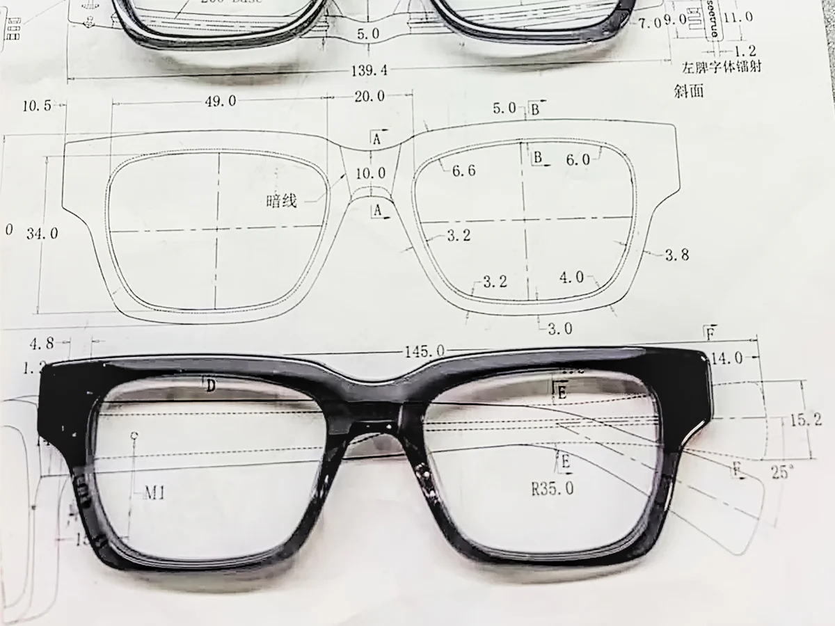 Black acetate eyeglass frame positioned over a dimensioned technical drawing showing its front shape and lens openings